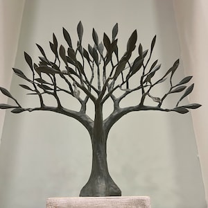 May include: A gray metal sculpture of a tree with a wooden base. The tree has many branches and leaves. The base is made of wood and has a light brown color.