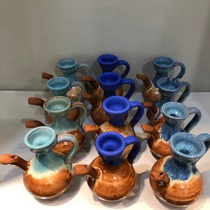 May include: A collection of small ceramic jugs with blue and brown glaze. The jugs have a spout and a handle. They are arranged in a row on a white surface.