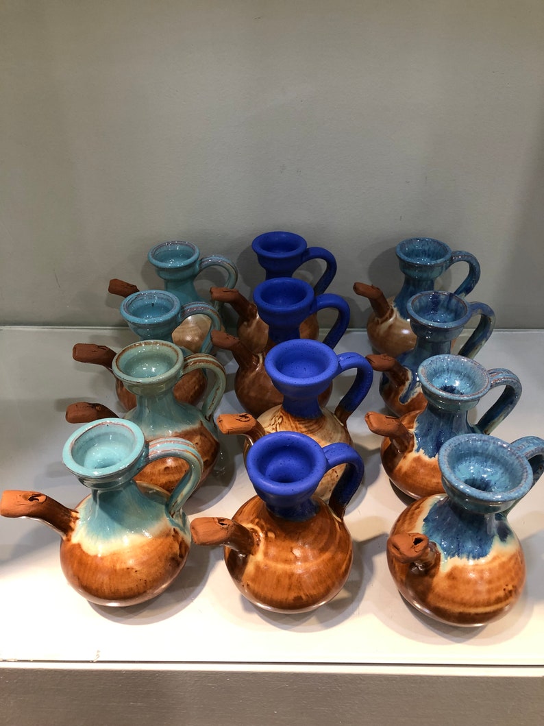 May include: A collection of small ceramic jugs with blue and brown glaze. The jugs have a spout and a handle. They are arranged in a row on a white surface.
