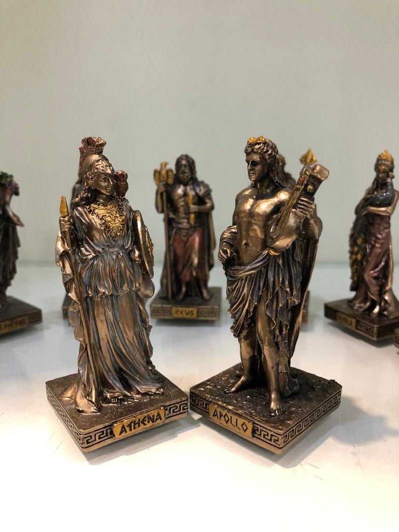 May include: Bronze figurines of Athena and Apollo, Greek gods, standing on bases with their names inscribed. The figurines are detailed and have a golden finish.