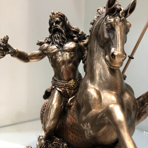 K&ouml;nnte beinhalten: Bronzefarbene Statue eines muskul&ouml;sen Mannes mit Bart und Krone, der ein Seepferd reitet. Der Mann h&auml;lt einen Dreizack. Das Seepferdchen hat eine flie&szlig;ende M&auml;hne und Schuppen. Detaillierte Merkmale.