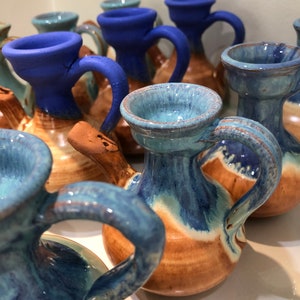 May include: A collection of small, hand-painted ceramic pitchers with blue and brown glaze. The pitchers have a unique shape with a spout and a handle.
