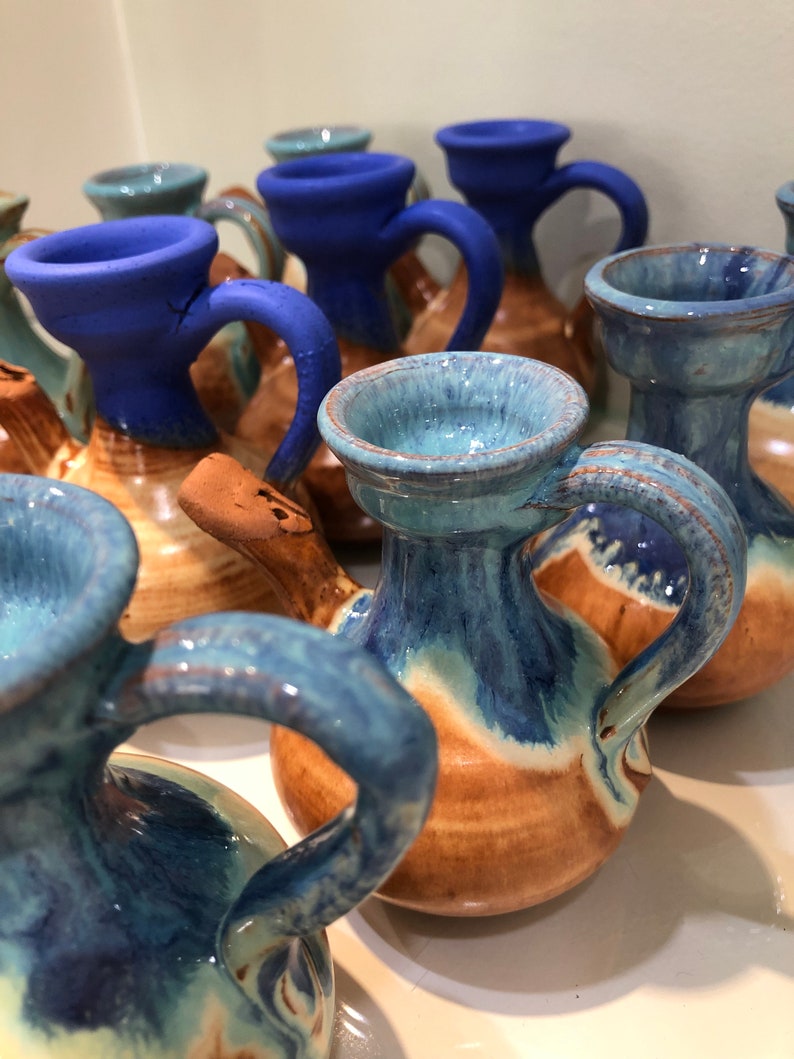 May include: A collection of small, hand-painted ceramic pitchers with blue and brown glaze. The pitchers have a unique shape with a spout and a handle.