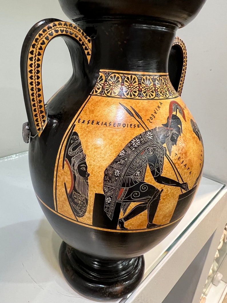 May include: Black and orange Greek amphora with two handles, a black and white painted scene of a warrior and a woman, and the text "EXSEKIASEMOIESE" and "TESANAPA".
