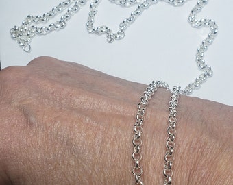 Puede incluir: Dos cadenas de plata, una encima de la otra, están envueltas alrededor de la muñeca de una persona. Las cadenas están hechas de pequeños eslabones redondos.