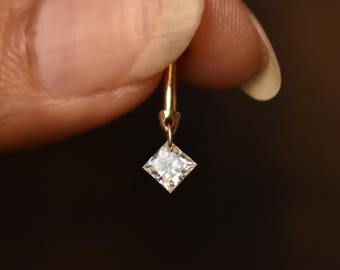 May include: A gold earring with a small, square-shaped diamond dangling from it.