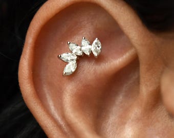 May include: A close-up of a silver ear piercing with a cluster of marquise-shaped clear stones in a leaf-like design.