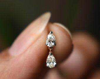 May include: A pair of pear-shaped diamond earrings dangle from a delicate chain. The earrings are held in a hand, showcasing their elegant design.