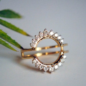 May include: A gold ring with a delicate, open circle design. The ring is set with small, sparkling diamonds that form a halo around the circle.