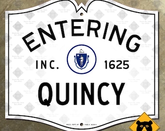 Könnte beinhalten: Weißes Schild mit schwarzem Text „ENTERING QUINCY“, „INC. 1625“ und einem kreisförmigen Emblem. Ein gelbes Diamantschild mit einer Bärgrafik befindet sich in der unteren rechten Ecke. Das Schild ist ein Schild des Massachusetts Department of Public Works.