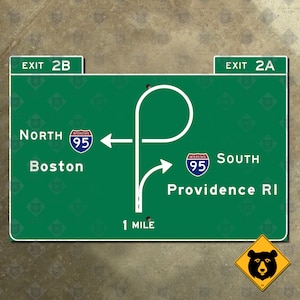 May include: Green road sign with white text and arrows indicating directions for Interstate 95 North to Boston and Interstate 95 South to Providence, Rhode Island. The sign also includes the text "Exit 2B" and "Exit 2A" and "1 Mile".