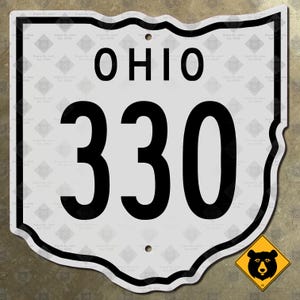 Könnte beinhalten: Ein weißes Metall-Straßenschild in Form des Bundesstaates Ohio mit schwarzem Rand. Das Wort OHIO ist oben in Schwarz aufgedruckt, und die Zahl 330 steht in großen schwarzen Ziffern darunter. Es gibt zwei kleine Befestigungslöcher oben und unten.