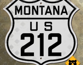 Könnte beinhalten: Ein weißes Metallschild mit schwarzem Text und Rand. Das Schild ist schildförmig und hat oben ein Loch. Der Text auf dem Schild lautet "MONTANA US 212".