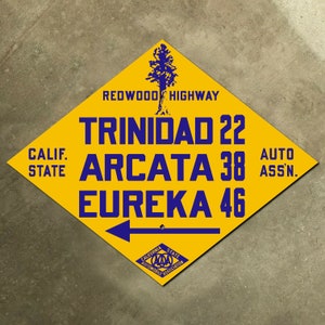 May include: A yellow diamond-shaped sign with blue text and a blue tree silhouette. The sign reads "Redwood Highway", "Trinidad 22", "Arcata 38", "Eureka 46", "Calif. State", and "Auto Assn."