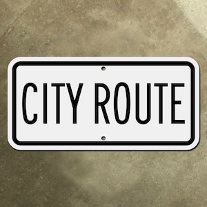 Może przedstawiać: Biały prostokątny znak z czarną ramką i czarnym tekstem, który brzmi "CITY ROUTE".