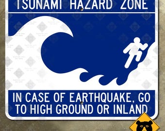 Könnte beinhalten: Rechteckiges blau-weißes Schild für die Tsunami-Gefahrenzone. Das Schild zeigt eine stilisierte Welle und eine Person, die bergauf rennt. Der Text auf dem Schild lautet: "IM FALL EINES ERDBEBENS, GEHEN SIE IN HOHES GELÄNDE ODER INS INNERE."