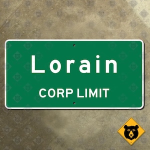 May include: A rectangular green sign with white text that reads "Lorain CORP LIMIT." The sign has a white border and two holes at the top. A yellow diamond sign with a black bear graphic is in the lower right corner.