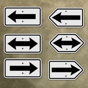 Może przedstawiać: Pięć białych znaków z czarnymi strzałkami wskazującymi w różnych kierunkach. Znaki są prostokątne i mają zaokrąglone rogi. Strzałki są wszystkie tego samego rozmiaru i kształtu.