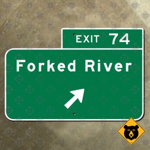May include: A green road sign with white text that reads "Forked River" and "Exit 74". A white arrow points to the right. A yellow bear warning sign is in the lower right corner. The background is a textured, neutral color.