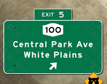 Op de afbeelding: Een groen verkeersbord met witte tekst met "EXIT 5" en "100". Het bord verwijst naar "Central Park Ave White Plains" met een witte pijl. Een geel waarschuwingsbord voor beren staat in de hoek.