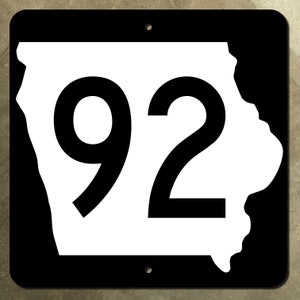 Pode incluir: Sinal de estrada de metal preto e branco com o número 92 e um contorno do estado de Iowa.