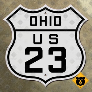 May include: White metal sign with black lettering. The sign is shaped like a shield and has the text "OHIO US 23" on it.