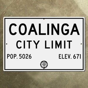 Può includere: Un cartello rettangolare bianco con testo nero che recita "Coalinga City Limit", "Pop. 5026" e "Elev. 671". Un sigillo in bianco e nero si trova nell'angolo in basso a destra.