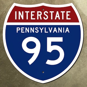 May include: A blue and red interstate highway sign with white text. The sign reads "Interstate Pennsylvania 95".