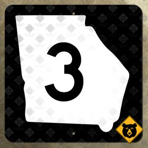 Puede incluir: Un cartel blanco con un contorno negro del estado de Georgia y el número 3 en negro. El cartel tiene un fondo negro y un pequeño cartel amarillo con un oso negro en la esquina inferior derecha.