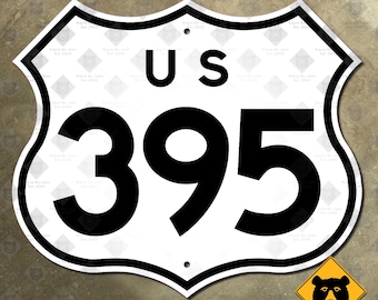 May include: A white US 395 highway sign with a black border and text. The sign has a shield shape with a small bear warning sign in the lower right corner. The sign is mounted on a neutral-colored surface.