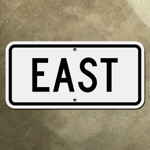 Może przedstawiać: Biały prostokątny znak z czarną ramką i czarnym napisem "WSCHÓD".