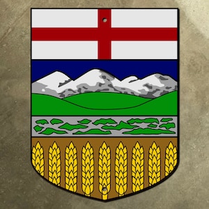 Op de afbeelding: Een blauw, groen en wit schildvormig embleem met een rood kruis, bergen, een rivier en tarwehalmen. Het embleem is het wapen van de Canadese provincie Alberta.