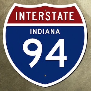 May include: A blue and red interstate highway sign with white text. The sign reads "INTERSTATE INDIANA 94".