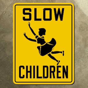 Può includere: Un cartello giallo con testo nero che dice "SLOW CHILDREN". Una silhouette nera di una ragazza con un vestito sta saltando in aria.