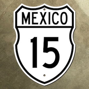 Può includere: Segnale stradale bianco e nero a forma di scudo con il testo "MEXICO" e il numero "15" in nero.