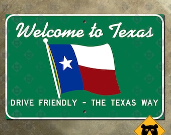 May include: A rectangular green metal sign with white text that reads "Welcome to Texas" and "Drive Friendly - The Texas Way." The Texas state flag is displayed on the sign. The sign has a white border and two holes for mounting.