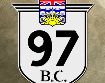 Op de afbeelding: Een wit schildvormig bord met zwarte letters en een blauwe en gele Canadese vlag. Het bord geeft "97 B.C."