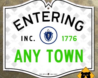 Könnte beinhalten: Ein weißes Metallschild mit geschwungener Oberkante, das den schwarzen Text ENTERING, den schwarzen Text INC., den grünen Text 1776 und den grünen Text ANY TOWN zeigt. Ein blau-weißes Siegel des Bundesstaates Massachusetts ist zentriert.