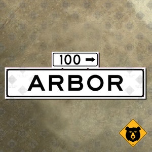 Puede incluir: Un cartel de calle blanco con texto negro que dice "ARBOR" con un cartel blanco más pequeño encima que dice "100 ->".