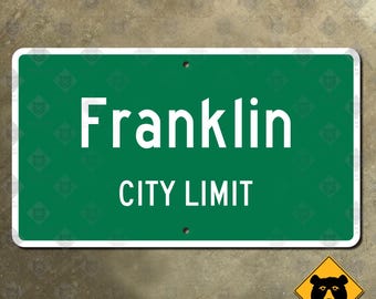 Könnte beinhalten: Ein rechteckiges grünes Schild mit weißem Text "Franklin CITY LIMIT". Das Schild hat einen weißen Rand und zwei kleine Löcher. Ein gelbes Bärenwarnschild befindet sich in der unteren rechten Ecke.