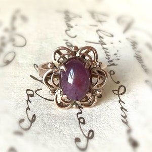 May include: A delicate gold ring with a purple gemstone set in a floral design.
