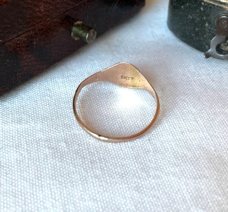 May include: A gold ring with a triangular face and a rounded band. The ring has the letters "SCT" engraved on the face. The ring is set against a white background.