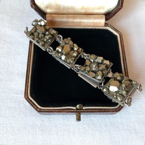 May include: A vintage bracelet featuring square silver links, each holding a cluster of pyrite stones. The bracelet is displayed inside a brown jewelry box with a black velvet interior, set against a white background.