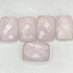 May include: Five pale pink, translucent, cushion-cut gemstones with faceted surfaces arranged in a cluster. Each stone features a rectangular shape with rounded corners and a polished finish that reflects light across the multiple geometric facets.