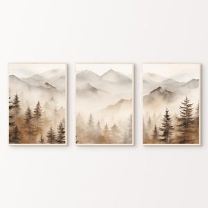 Könnte beinhalten: Ein Set aus drei Aquarelldrucken mit einer nebeligen Berglandschaft in Braun- und Grautönen. Die Drucke zeigen einen Wald mit Kiefern im Vordergrund und eine Bergkette im Hintergrund.
