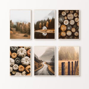 Könnte beinhalten: Sechs gerahmte Kunstdrucke mit herbstlichen Szenen. Die Bilder zeigen einen Wald, eine Hütte am See, einen Holzstapel, eine Kürbissammlung, eine kurvenreiche Straße und einen rustikalen Zaun auf einem Feld. Die Farbpalette ist warm mit Erdtönen.