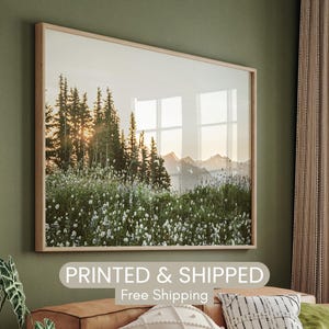 May include: A framed photograph of a mountain landscape with a forest in the foreground and a sunset in the background. The photo is printed on high-quality paper and framed in a natural wood frame.