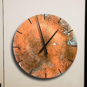 May include: A round, copper-colored clock with black hands and a distressed, textured surface. The clock is mounted on a white wall.