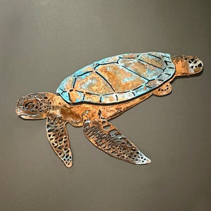Puede incluir: Un recorte de metal de una tortuga marina con una pátina marrón oxidada y azul. La tortuga está nadando con la cabeza y las aletas extendidas.