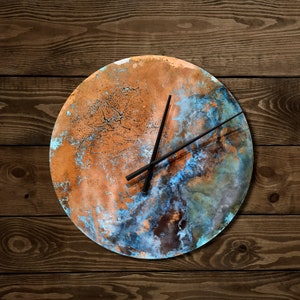 May include: A round copper clock with a blue and brown marbled design. The clock has black hands and is set to 3:00.